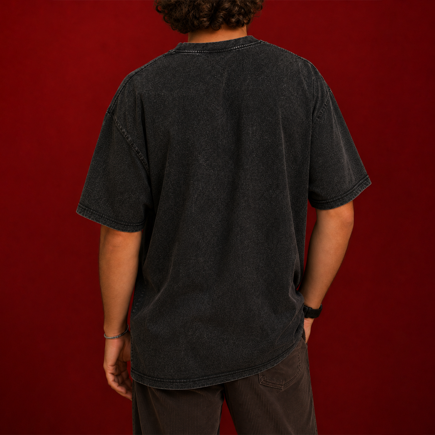 A person shown from the back wearing an oversized faded black t-shirt and dark brown pants, standing against a solid dark red background.