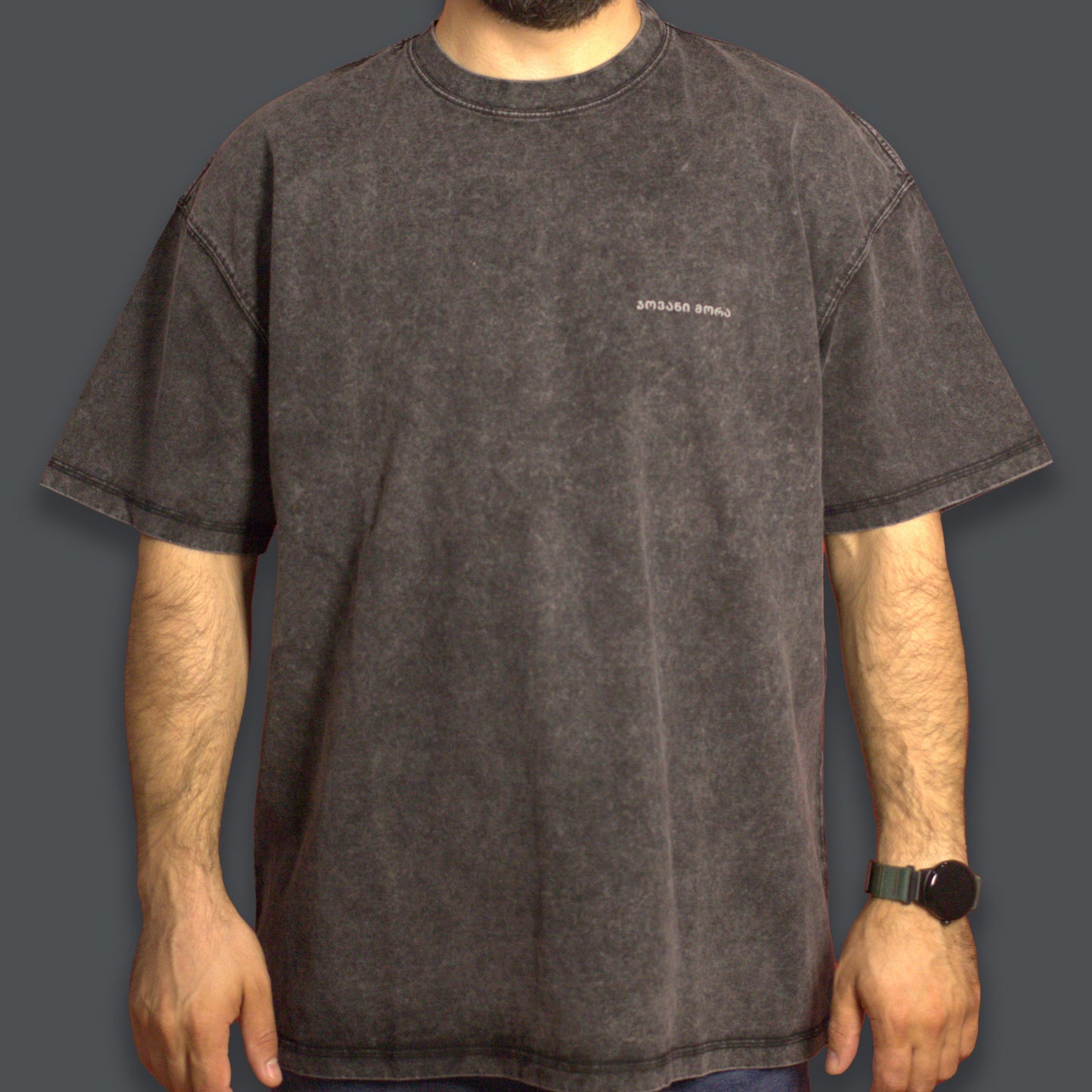 Person wearing a black acid-washed T-shirt with a tonal Georgian logo