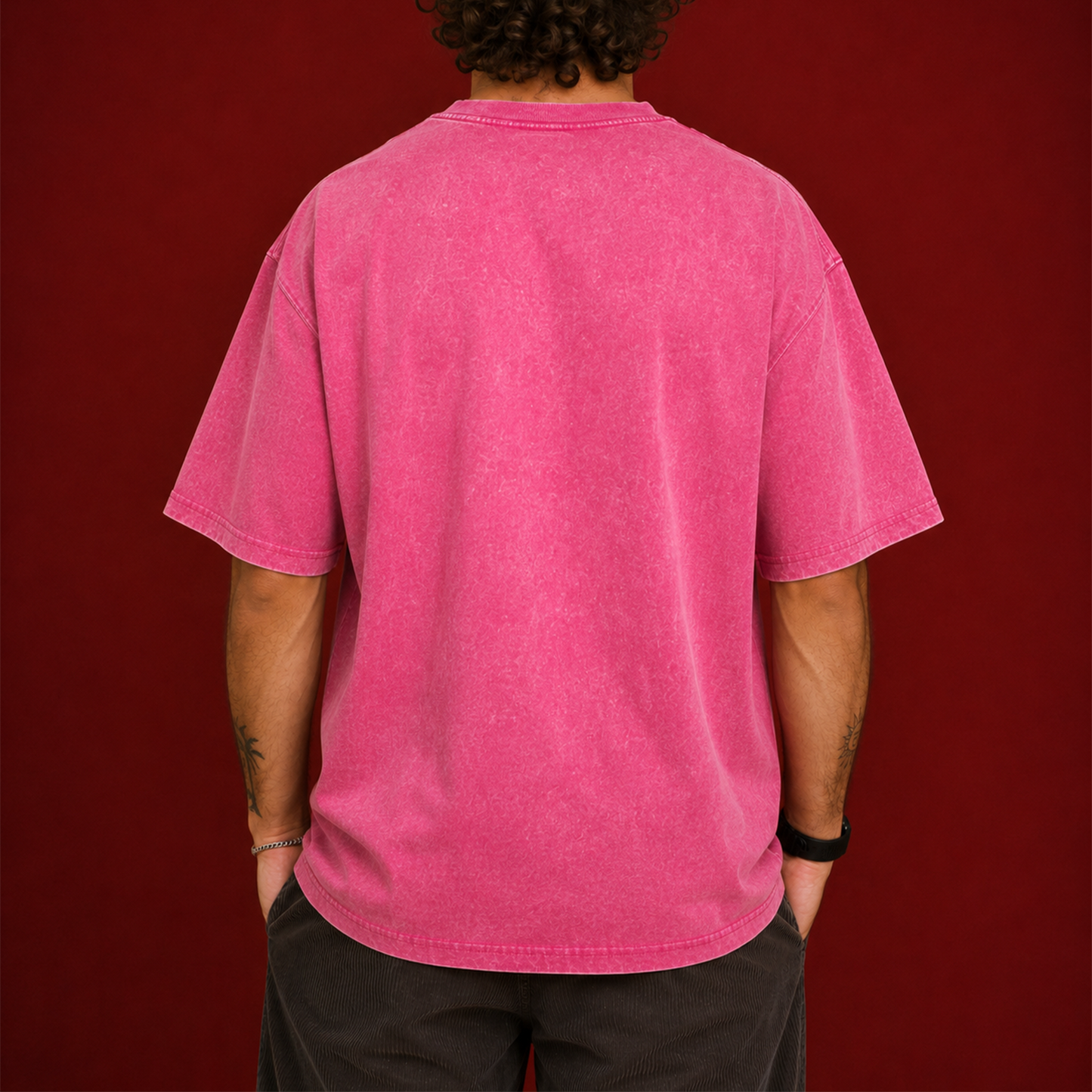 A person viewed from the back wearing an oversized short-sleeve t-shirt in a washed, faded pink, set against a solid dark red background.