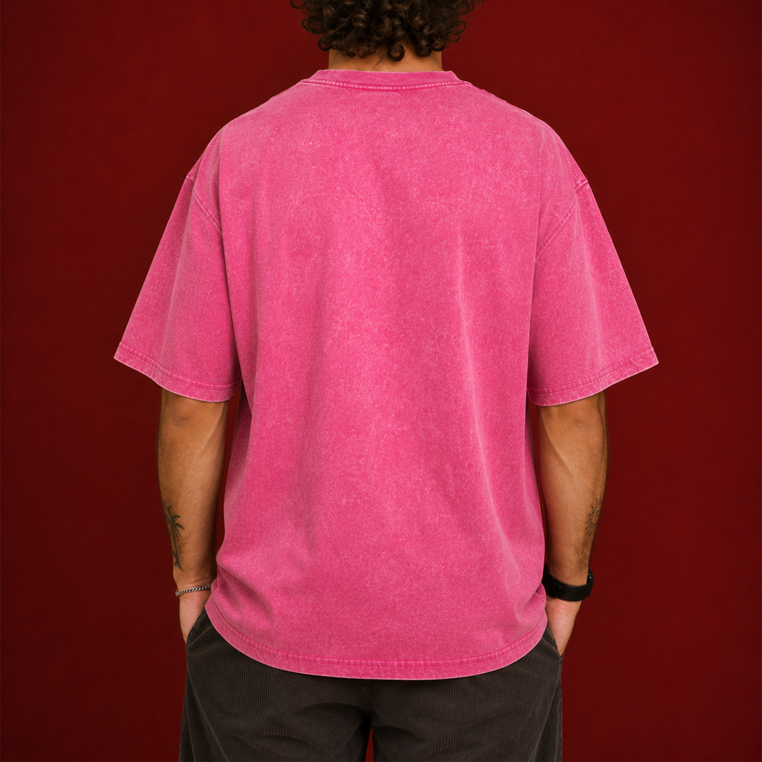 A person viewed from the back wearing an oversized short-sleeve t-shirt in a washed, faded pink, set against a solid dark red background.