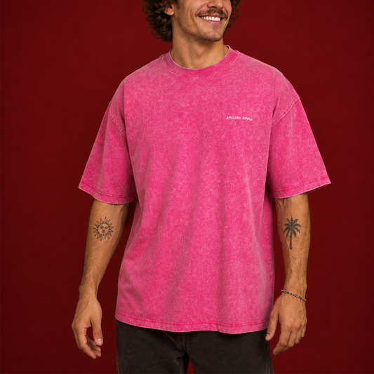 A man wearing a bright pink mineral-wash t-shirt with a small white 'SPIRIT' logo on the left chest, posed against a solid dark red background.