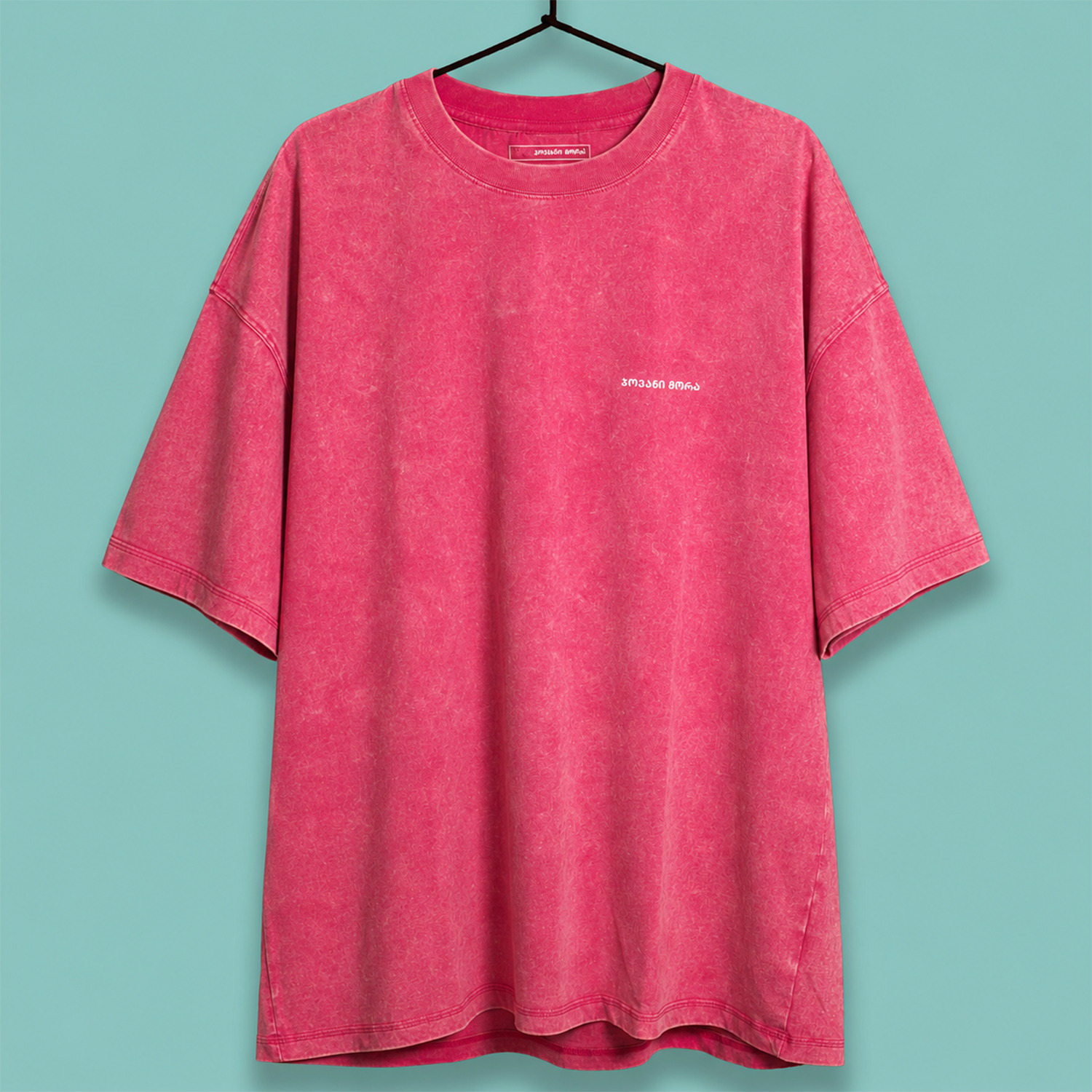 A washed pink short-sleeve t-shirt with a small white 'Philadelphia Phillies' logo on the left chest, hanging on a black hanger against a solid teal background.
