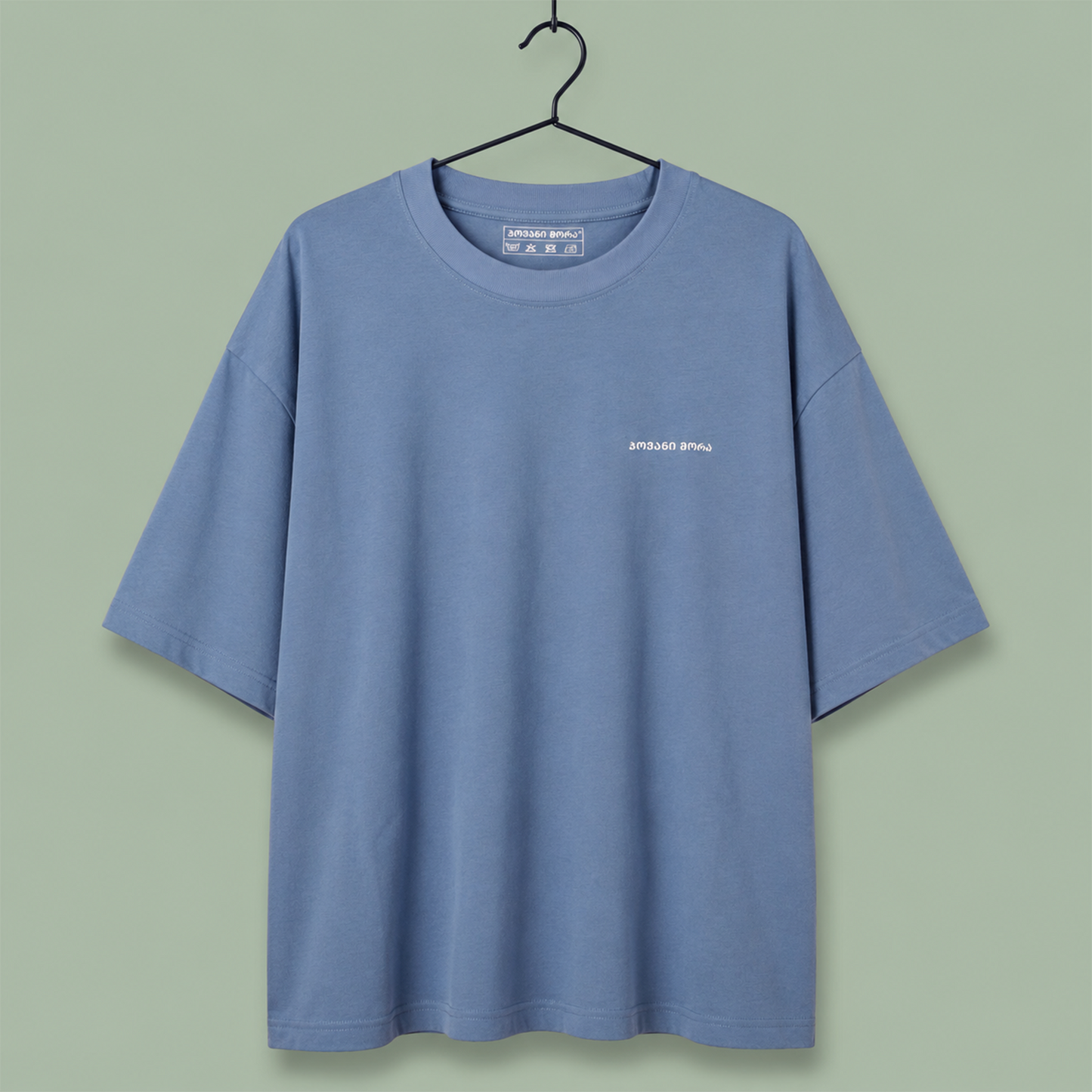 light blue crewneck t-shirt with a small white 'SPEED SHOP' logo on the left chest, set against a solid sage green background.