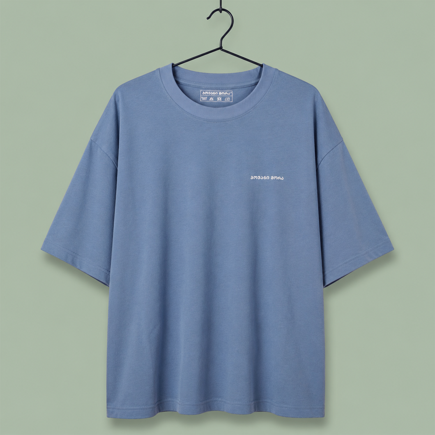 light blue crewneck t-shirt with a small white 'SPEED SHOP' logo on the left chest, set against a solid sage green background.