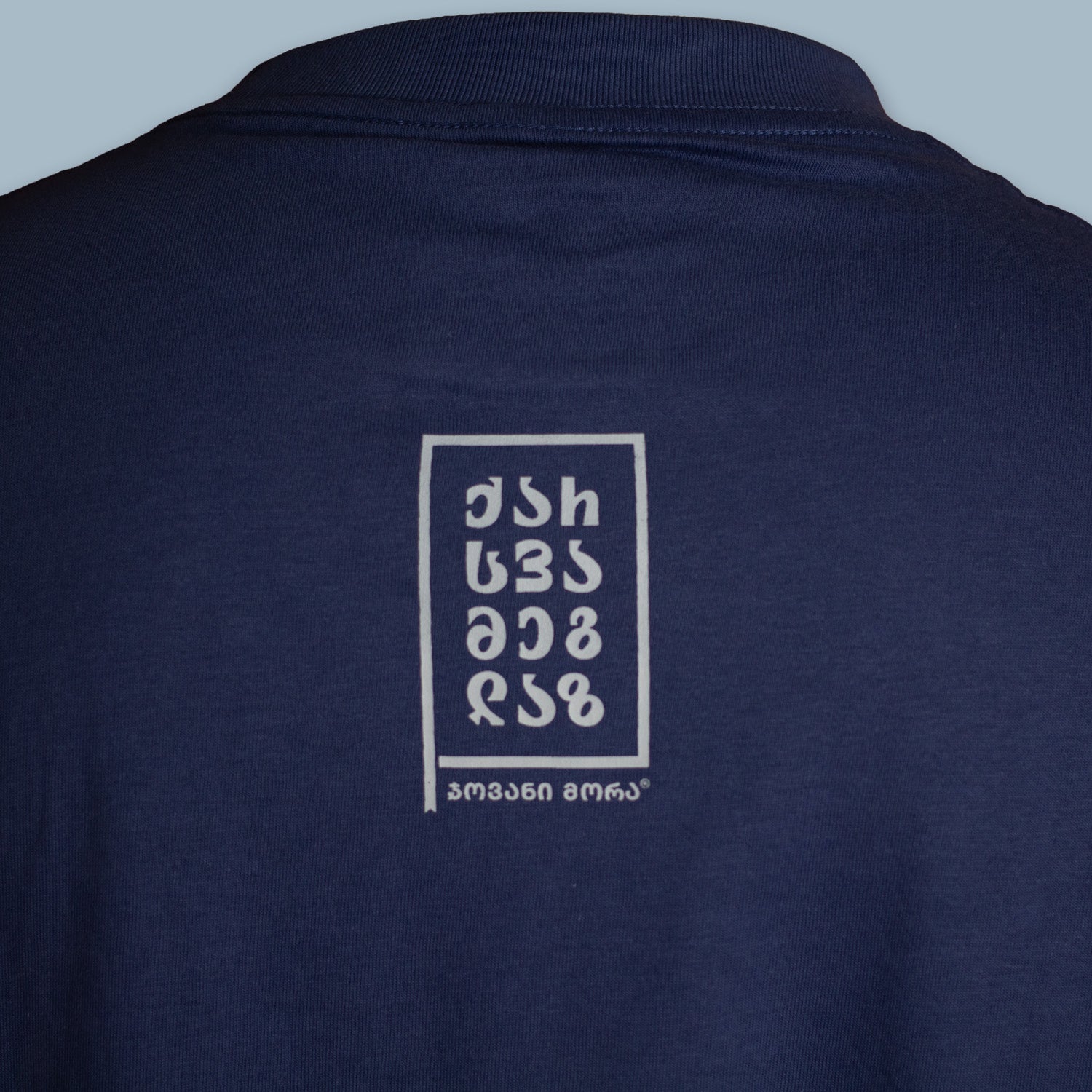 Close-up of a small white typographic graphic on the back of a navy T-shirt