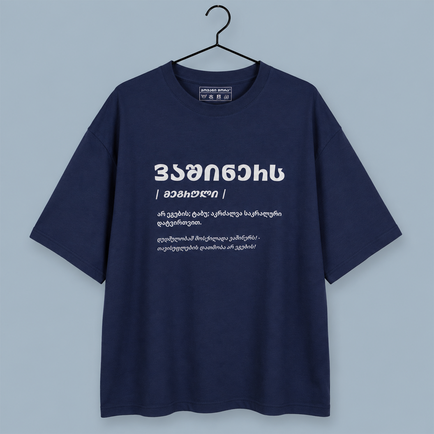 A navy blue short-sleeve t-shirt hanging on a black hanger against a light blue-gray background. The shirt features white Georgian text printed on the chest.