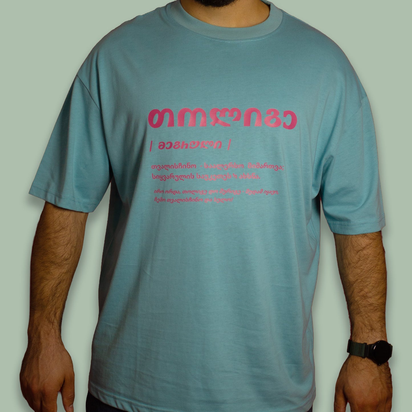Person wearing a pale green Tholige T-shirt with red front text