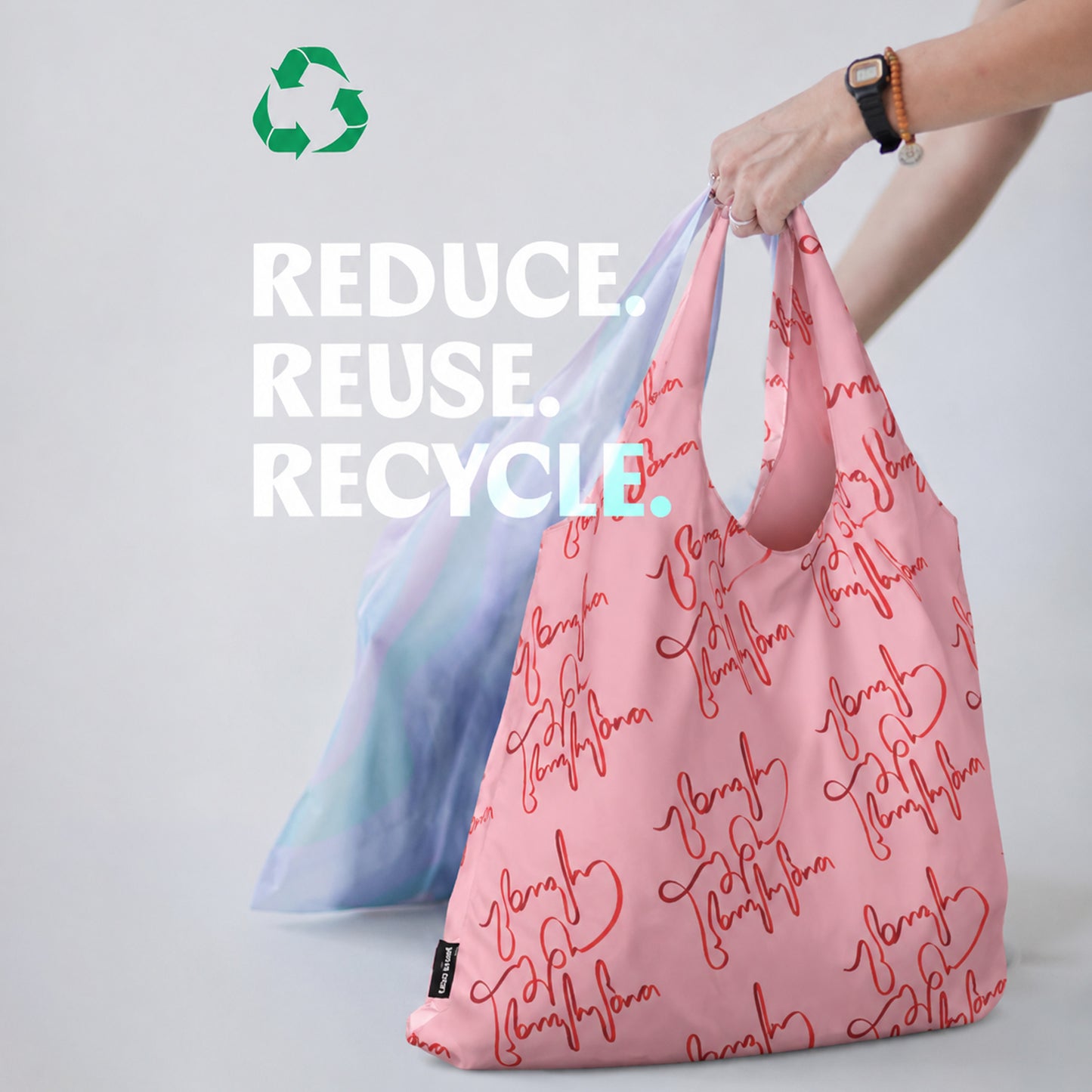 Pink reusable bag with text and blue gradient bag, with 'Reduce. Reuse. Recycle.' text and recycling symbol.