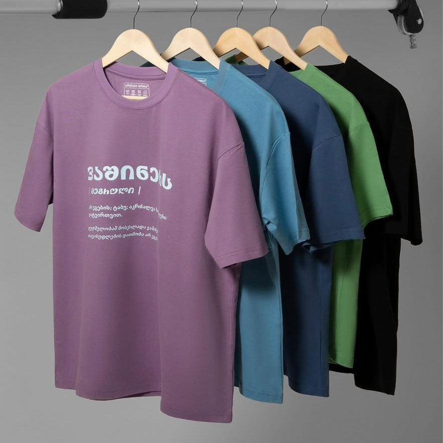 Linguistic Diversity T-shirts in several colors displayed on wooden hangers
